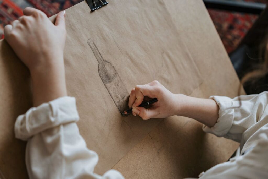 Apprendre à dessiner sans se ruiner : par où commencer quand on part de zéro personne qui dessine une bouteille au crayon sur du papier kraft