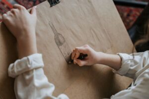 personne qui dessine une bouteille au crayon sur du papier kraft